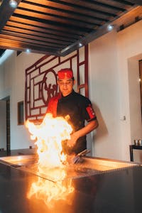 Chef performing a hibachi style cooking with fire on grill in a modern indoor restaurant setting.