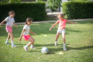 Three young girls having fun playing soccer outdoors on a sunny day.