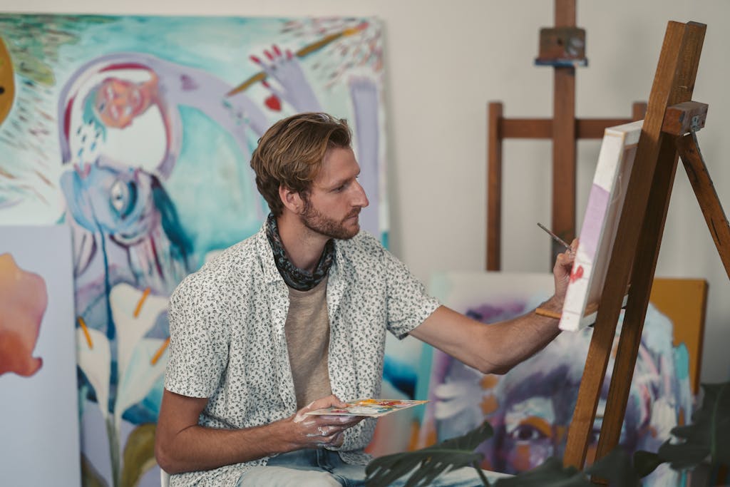 Caucasian male artist focusing on a colorful painting in a modern art studio.
